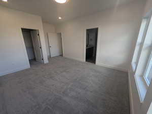 Unfurnished bedroom with a closet, a walk in closet, ensuite bathroom, and carpet