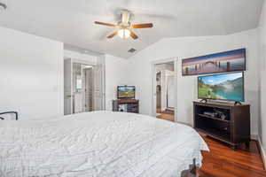 Bedroom with dark hardwood / wood-style flooring, ensuite bathroom, vaulted ceiling, and ceiling fan