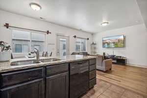 Kitchen featuring sink, black dishwasher, light stone countertops, and light hardwood / wood-style flooring