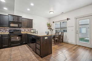 Kitchen with kitchen peninsula, black appliances, light stone counters, light hardwood / wood-style floors, and tasteful backsplash