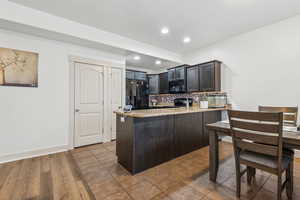 Kitchen with kitchen peninsula, tasteful backsplash, wood-type flooring, black appliances, and light stone counters