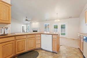 Kitchen with light brown cabinets, hanging light fixtures, kitchen peninsula, sink, and white appliances