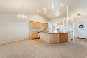 Kitchen with light brown cabinets, a kitchen island, vaulted ceiling, light colored carpet, and white appliances