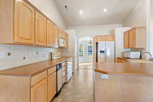 Kitchen featuring lofted ceiling, kitchen peninsula, sink, light brown cabinetry, and white appliances