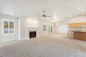 Unfurnished living room with lofted ceiling, light carpet, a tiled fireplace, and ceiling fan