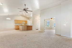 Unfurnished living room featuring sink, light carpet, high vaulted ceiling, and ceiling fan with notable chandelier