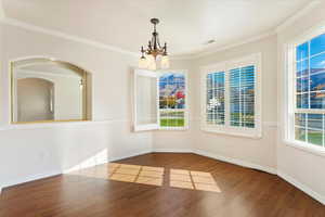 Empty room featuring crown molding, wood-type flooring, and a chandelier