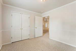 Unfurnished bedroom featuring a closet, ornamental molding, and light colored carpet