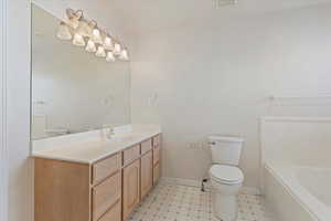 Bathroom with toilet, a tub to relax in, vanity, and tile patterned flooring