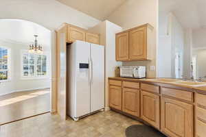 Kitchen with light brown cabinets, sink, decorative light fixtures, an inviting chandelier, and white appliances