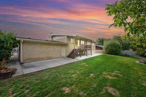 Back house at dusk with a patio area and a lawn