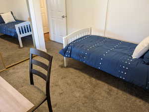 Main level second bedroom featuring dark colored carpet and multiple windows featuring a closet and carpet