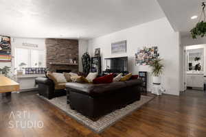 Living room featuring vaulted ceiling, a stone fireplace, a textured ceiling, and dark hardwood / wood-style flooring