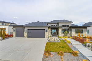 Prairie-style home with an attached garage, board and batten siding, driveway, a front lawn, and stone siding