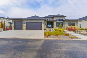 Prairie-style house featuring a shingled roof, an attached garage, concrete driveway, and stone siding
