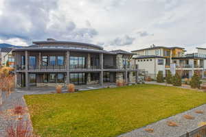 Rear view of property with stone siding, a lawn, a patio, and a balcony