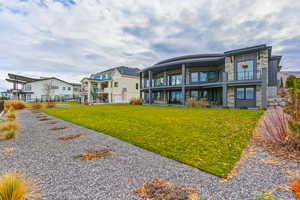 Back of house featuring stone siding, a balcony, and a lawn