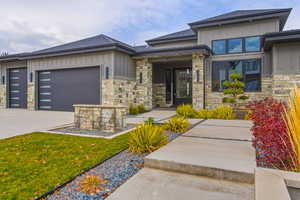 View of front of home with board and batten siding, stone siding, a shingled roof, an attached garage, and driveway