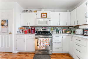 Kitchen with light hardwood / wood-style flooring, white cabinets, stainless steel range with gas cooktop, and tasteful backsplash