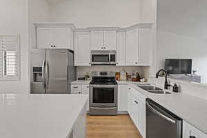 Kitchen featuring sink, light wood-type flooring, stainless steel appliances, vaulted ceiling, and white cabinets