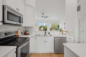 Kitchen with backsplash, white cabinetry, light hardwood / wood-style flooring, sink, and stainless steel appliances