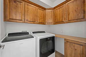 Clothes washing area featuring hardwood / wood-style floors, washing machine and clothes dryer, and cabinets