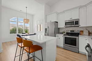 Kitchen featuring hanging light fixtures, appliances with stainless steel finishes, light wood-type flooring, and white cabinets