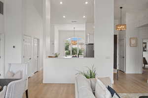 Interior space with stainless steel fridge, light wood-type flooring, a high ceiling, pendant lighting, and a notable chandelier