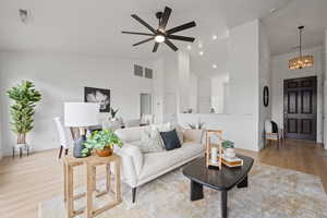 Living room with high vaulted ceiling, ceiling fan with notable chandelier, and light wood-type flooring