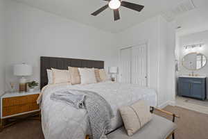 Bedroom with a closet, light carpet, ensuite bath, sink, and ceiling fan