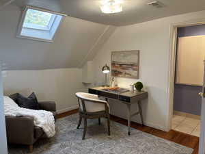 Office featuring lofted ceiling with skylight,  light wood-type flooring and attached full bathroom