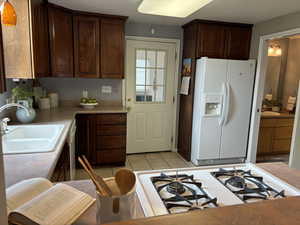 Kitchen featuring white dishwasher, sink, light tile patterned floors, and white fridge with ice dispenser