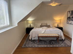 Upstairs bedroom featuring lofted ceiling and dark hardwood style flooring & king sized bed