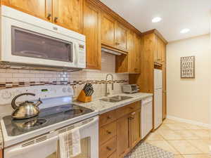 Kitchen featuring decorative backsplash, light tile patterned floors, light stone countertops, sink, and white appliances