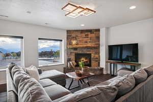 Living room with a stone fireplace, a textured ceiling, a healthy amount of sunlight, and dark hardwood / wood-style flooring