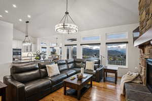 Living room featuring high vaulted ceiling, hardwood / wood-style flooring, and a stone fireplace