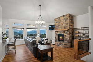 Living room with lofted ceiling, hardwood / wood-style floors, a notable chandelier, and a fireplace