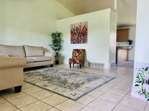 Living area featuring light tile patterned flooring, visible vents, and a towering ceiling