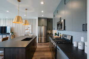 Kitchen featuring dark wood-type flooring, a center island, pendant lighting, appliances with stainless steel finishes, and tasteful backsplash