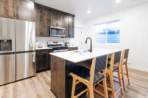 Kitchen with sink, an island with sink, a kitchen breakfast bar, stainless steel appliances, and light hardwood / wood-style flooring