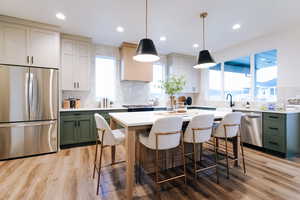 Kitchen with appliances with stainless steel finishes, light wood-type flooring, green cabinets, decorative light fixtures, and decorative backsplash