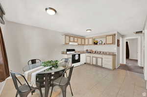 Kitchen featuring white electric range, light brown cabinetry, sink, and light tile patterned floors