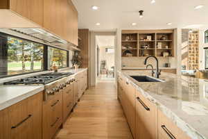 Kitchen with sink, light stone countertops, stainless steel gas stovetop, and light wood-type flooring