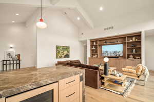 Living room featuring beamed ceiling, high vaulted ceiling, light hardwood / wood-style floors, and beverage cooler