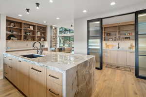 Kitchen with light hardwood / wood-style floors, light stone countertops, sink, and a kitchen island with sink