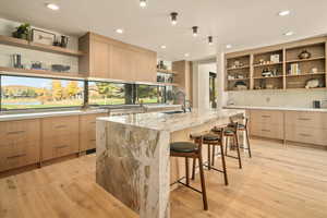 Kitchen with a center island with sink, a breakfast bar, light stone counters, and light wood-type flooring