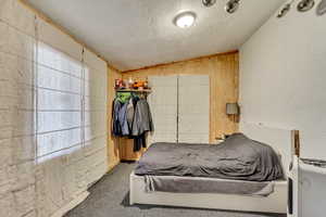 Carpeted bedroom with lofted ceiling, a textured ceiling, and wood walls