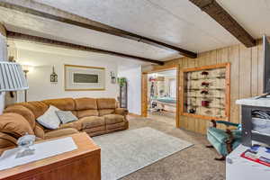 Living room featuring beamed ceiling, light carpet, a textured ceiling, and wood walls