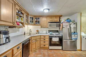 Kitchen with washer / dryer, light tile patterned floors, appliances with stainless steel finishes, a textured ceiling, and sink