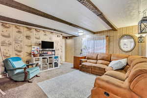 Living room with beamed ceiling, wooden walls, and carpet flooring